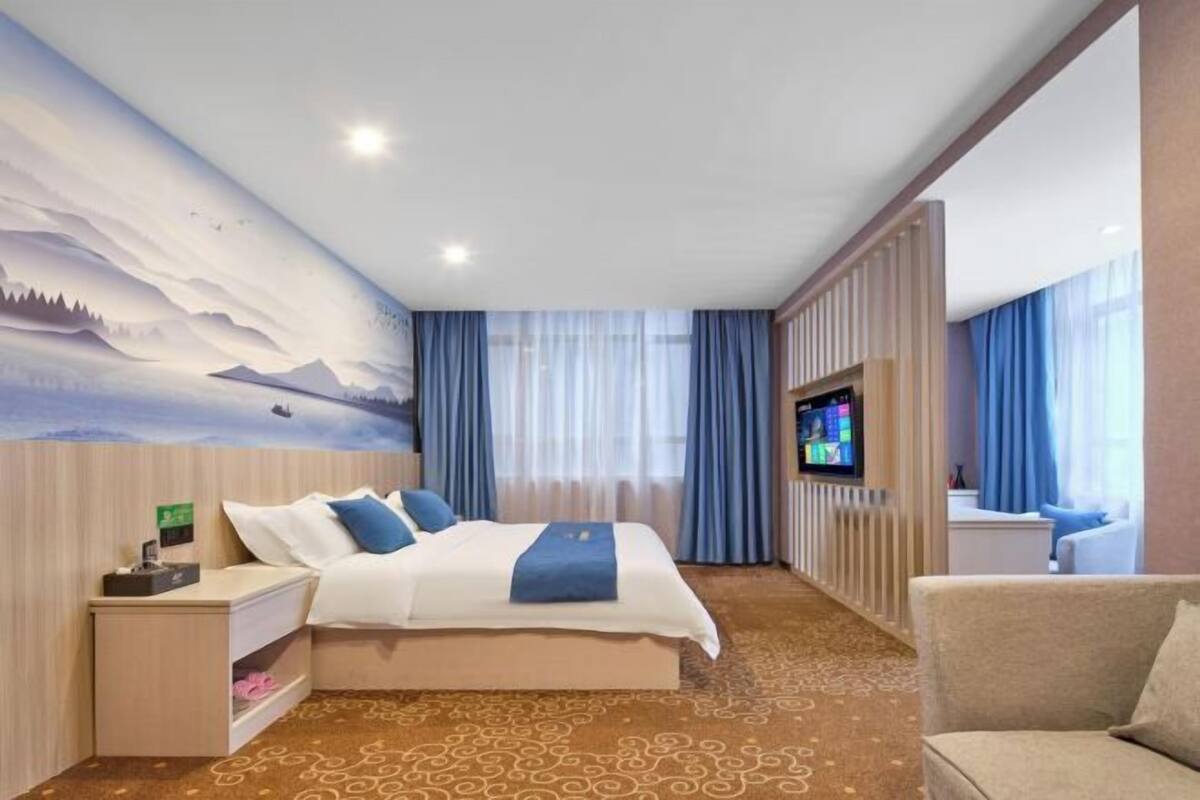 A hotel room with a bed, a TV, a sofa, a nightstand, and a wall mural.
