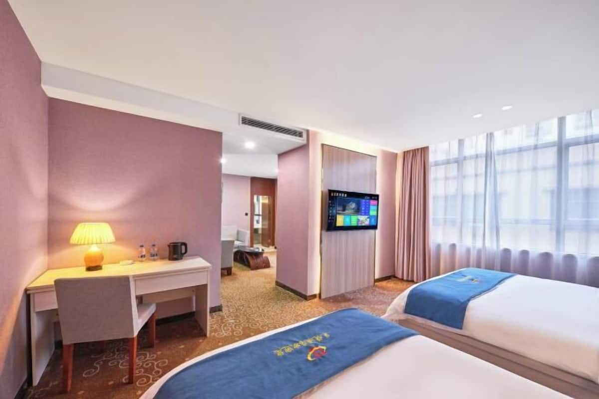 A hotel room with a desk, chair, bed, TV, and large windows.