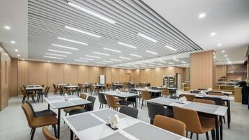 A modern dining area with tables and chairs, a high ceiling with linear lighting, and a kitchen area in the background.