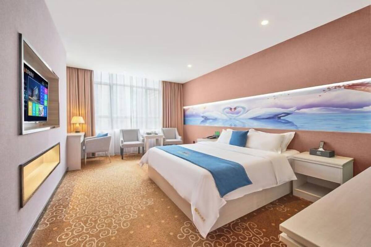 A hotel room with a large bed, a desk, a chair, a TV, and a painting on the wall.