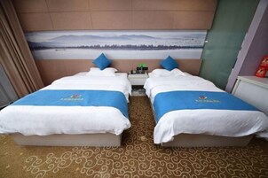 Quarto de hotel com duas camas, uma mesa de cabeceira, um quadro de uma paisagem e um tapete estampado.