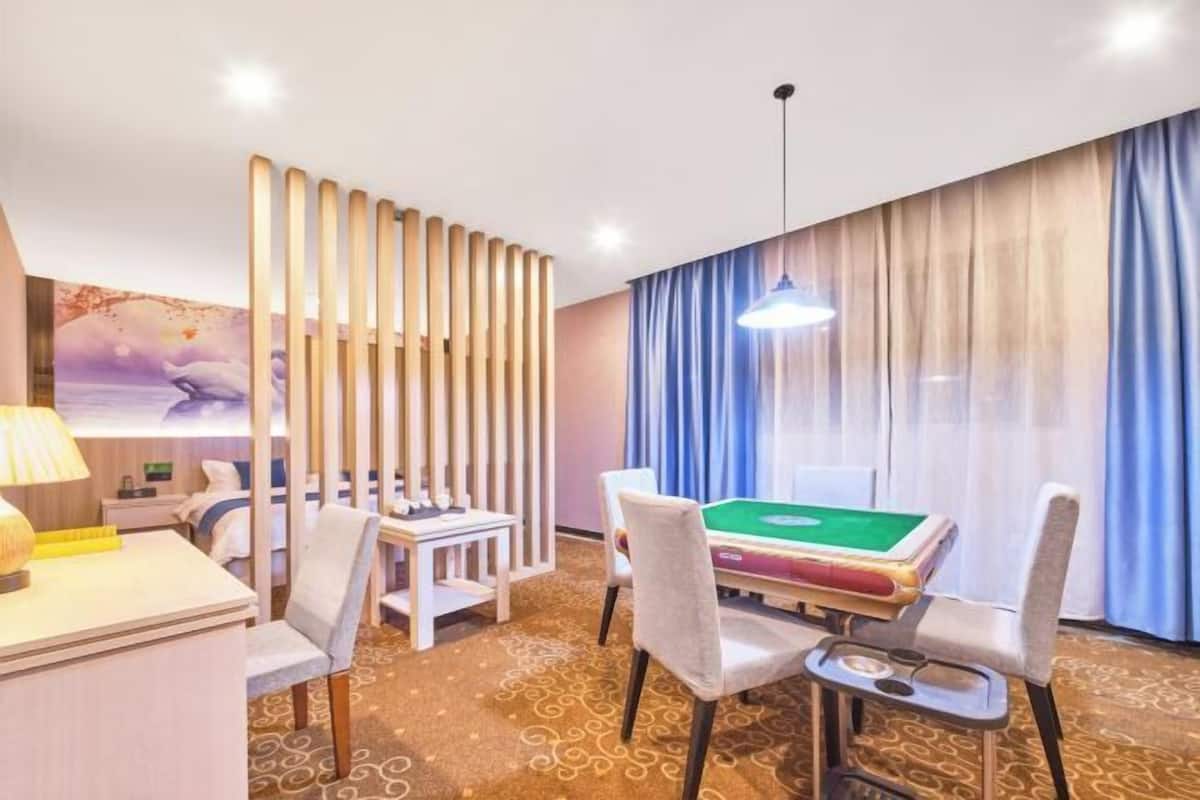 A hotel room with a pool table, a desk, a chair, a lamp, a decorative wall, and a window with curtains.