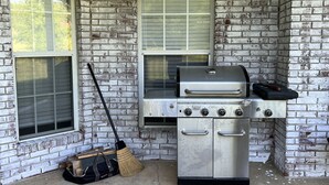 Fachada de ladrillo con cocina exterior de acero inoxidable, que incluye una parrilla y un horno, y una escoba apoyada en la pared.