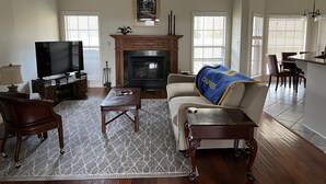 Un salón amplio con chimenea, televisión y comedor, con una cocina al fondo.