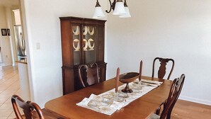 Una mesa de comedor con seis sillas, un aparador de madera con puertas de cristal y una araña.