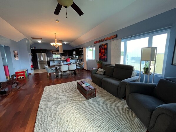 A spacious living room with a large gray sofa, a coffee table, and a dining area with a kitchen in the background. - MODERN HILLTOP FAMILY HOME (Warwick)