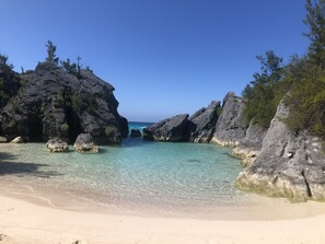 A beach with clear turquoise water, rocky formations, and sparse vegetation. - MODERN HILLTOP FAMILY HOME (Warwick)