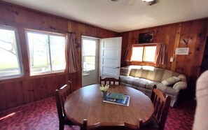 Una habitación con paredes de madera, una mesa redonda con sillas, un sofá y una puerta que da al exterior.