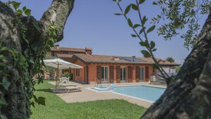 Una casa con piscina, rodeada de césped y árboles.