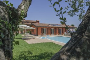 Una casa con piscina, rodeada de césped y árboles.