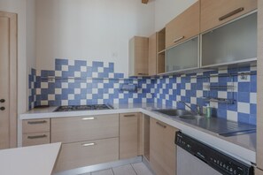 A modern kitchen with light wood cabinets, a blue and white checkered backsplash, stainless steel appliances, and a dishwasher. - La Casina Apartment - with garden and pool (Pozzolengo)