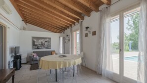 A spacious room with a wooden ceiling, a round table with chairs, a television, and a painting on the wall.