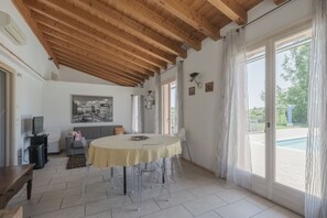 A spacious room with a wooden ceiling, a round table with chairs, a television, and a painting on the wall. - La Casina Apartment - with garden and pool (Pozzolengo)