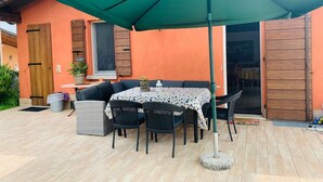 Un patio exterior con una mesa, sillas, un paraguas verde y una puerta de madera.