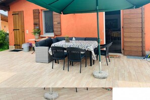 Un patio exterior con una mesa, sillas, un paraguas verde y una puerta de madera.