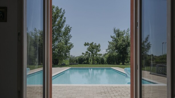 A swimming pool with a tiled deck, surrounded by trees and a clear sky.