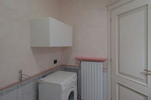 A compact laundry room with a washing machine, a radiator, and a white cabinet.