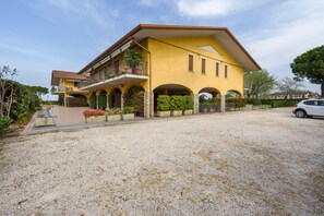 A yellow two-story house with a balcony, arched windows, and a gravel driveway.