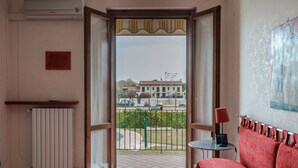 Ein Hotelzimmer mit Bett, Heizkörper, einem kleinen Tisch mit Lampe und Blick auf eine Straße und Gebäude.