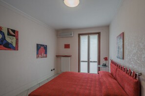 A bedroom with a large bed, a radiator, a small table with a lamp, and artwork on the walls.