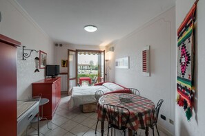 A compact room with a bed, a small dining table, a TV, and a balcony with a view.