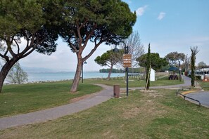 A park with a paved path, trees, a signpost, and a view of the sea.