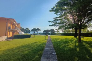 A pathway leading to a building with a balcony, surrounded by green grass and trees.
