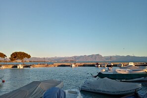 A marina with boats docked, a clear sky, and mountains in the background.