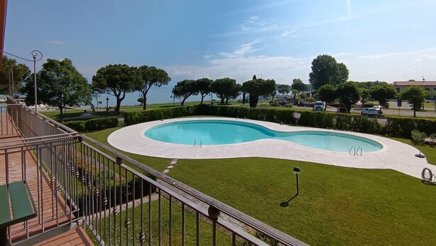 Ein Pool mit ungewöhnlicher Form, umgeben von gepflegtem Rasen und Bäumen, aufgenommen von einem Balkon aus.