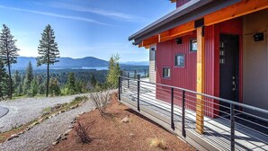 Un bâtiment moderne à la façade rouge et grise, doté d’un balcon avec une rambarde en métal, et offrant une vue sur une forêt et des montagnes en arrière-plan.