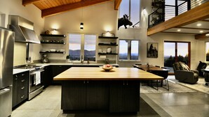 Une cuisine moderne dotée d’un grand îlot central, d’un plafond en bois et offrant une vue sur les montagnes grâce à de grandes fenêtres.