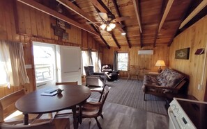 A wooden cabin interior with a dining table, chairs, a sofa, and a ceiling fan.