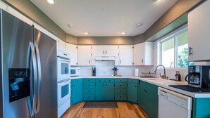 Een moderne keuken met blauwgroene kastjes, roestvrijstalen apparatuur en houten vloeren.