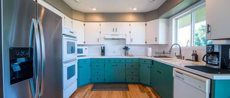 A modern kitchen with teal cabinets, stainless steel appliances, and wooden flooring.