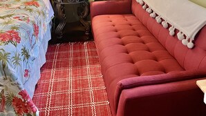 Une chambre à coucher avec un lit, un canapé rouge, une lampe, une grande plante et une fenêtre avec des rideaux.