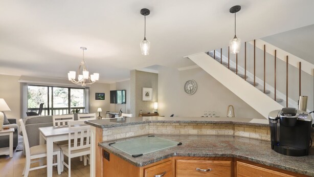 A modern kitchen with granite countertops, wooden cabinets, and a built-in island. There is a coffee maker on the island, and a staircase with a railing leading to another level. - 103 Golfmaster- 2 Bedroom Townhouse in Shipyard Ocean Front Community. Golf & Lagoon View Sleeps 6 (Hilton Head Island)