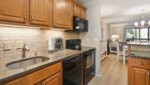 A kitchen with wooden cabinets, a brick backsplash, stainless steel appliances, and a bar area with stools. - 103 Golfmaster- 2 Bedroom Townhouse in Shipyard Ocean Front Community. Golf & Lagoon View Sleeps 6 (Hilton Head Island)