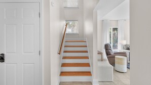 Un escalier avec des marches en bois menant à un palier, une porte blanche et un coin salon avec une chaise et une petite table.