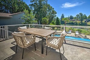 A wooden table with four wicker chairs on a balcony overlooking a swimming pool. - Luxe Getaway w/ Riverfront Views in Grants Pass! (Grants Pass)
