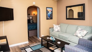 A living room with a sofa, coffee table, and a TV. There is a painting on the wall and a mirror above the sofa. - SB2-Downtown Munising, Deli and Brewery Across the Street (Munising)