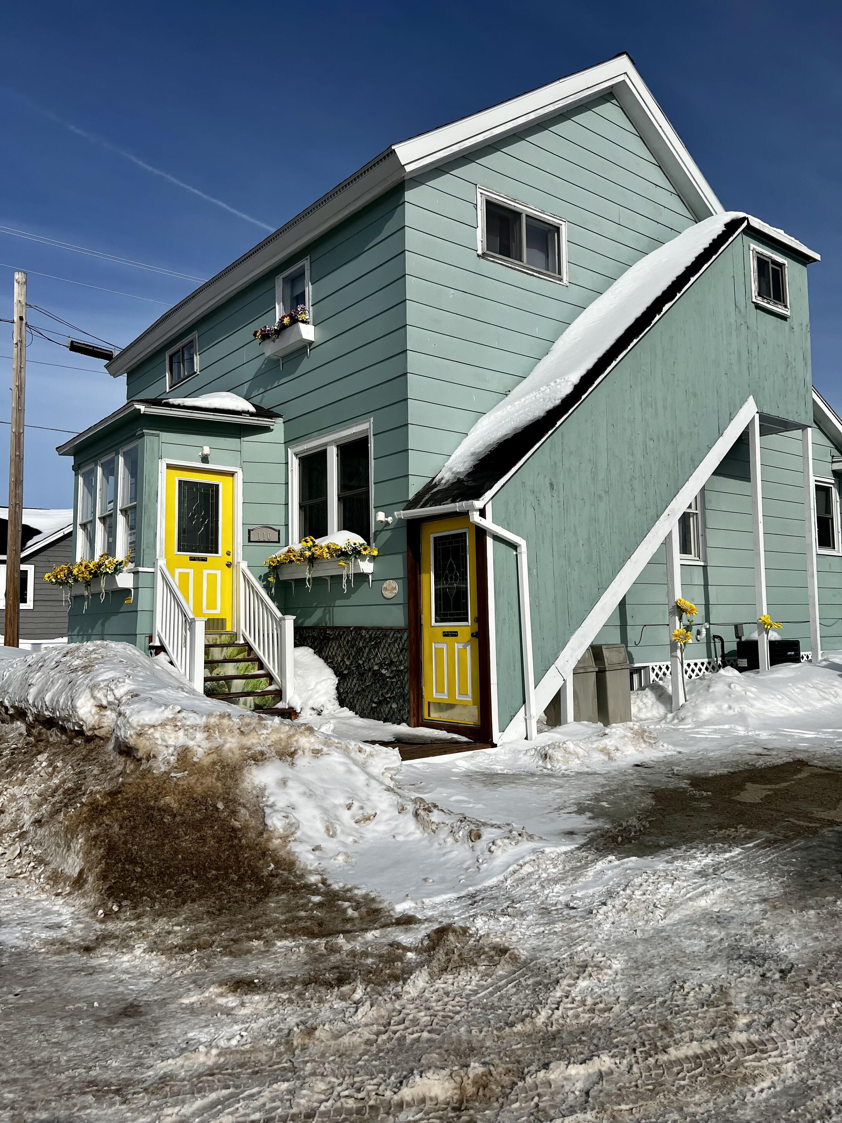 A two-story house with a green exterior and yellow doors, surrounded by snow.