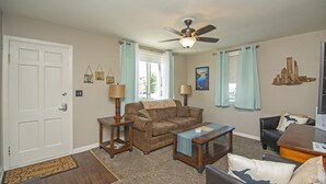 A living room with a ceiling fan, a sofa, a coffee table, and a side table with lamps. - Munising, Walk to Boat Cruises, Coffee Shops & Brewery! (Munising)
