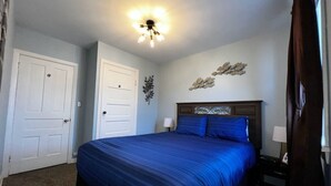 A bedroom with a large bed, two white doors, a ceiling light fixture, and a wall decoration. - Munising, Walk to Boat Cruises, Coffee Shops & Brewery! (Munising)