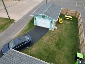 Edificio de una sola planta con garaje, entrada para vehículos, un coche y un pequeño patio cercado con banco y cortacésped.