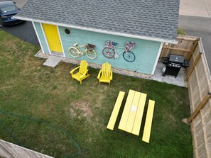 A house with a green exterior, a garage, a barbecue area, and a yard with yellow Adirondack chairs and a picnic table.