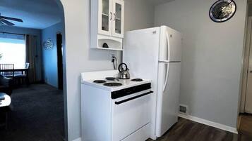 A compact kitchen with a white stove, a white refrigerator, and a white cabinet above the stove.