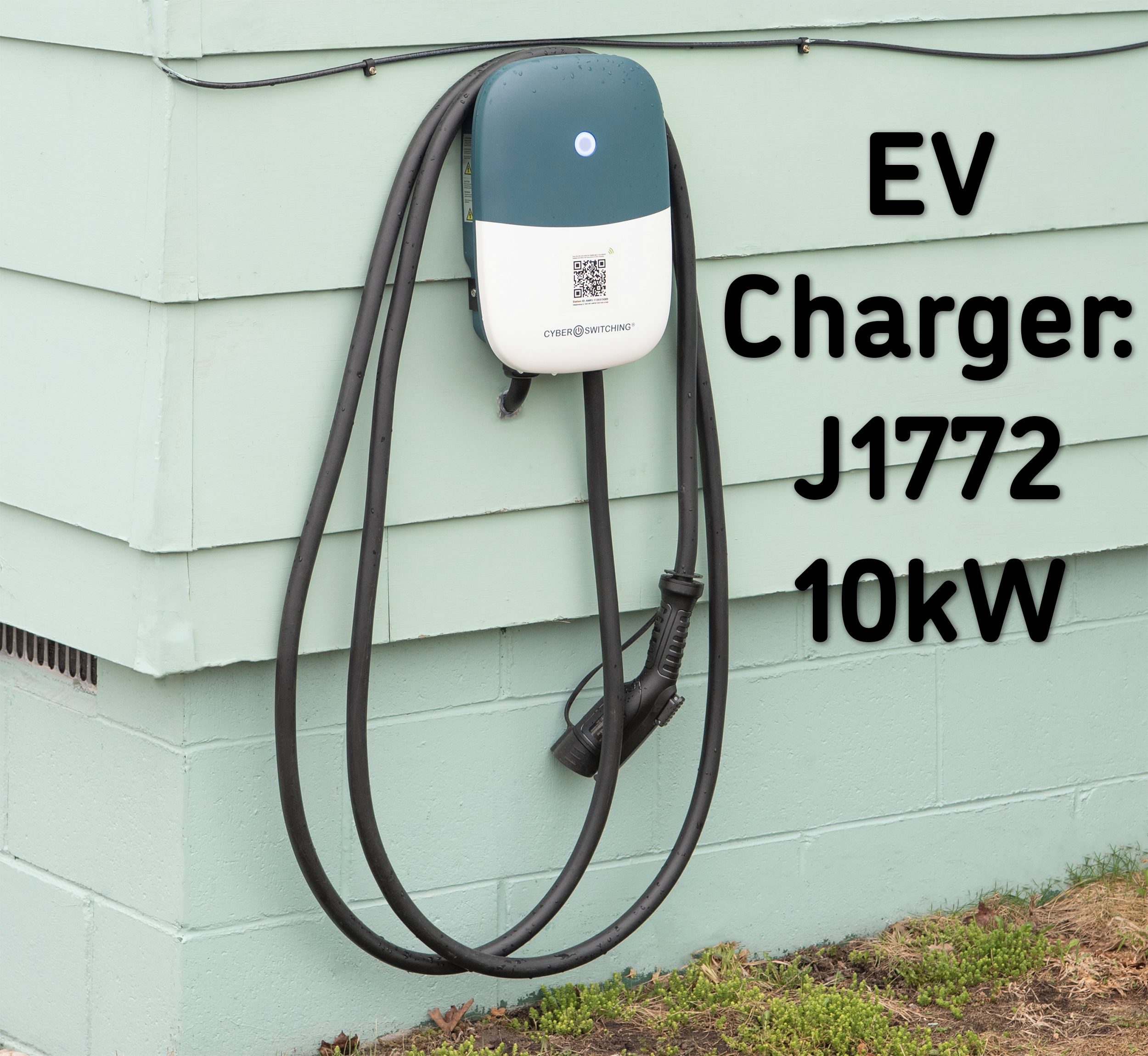 An EV charger labeled J1772 with a 10kW capacity attached to a light green building.
