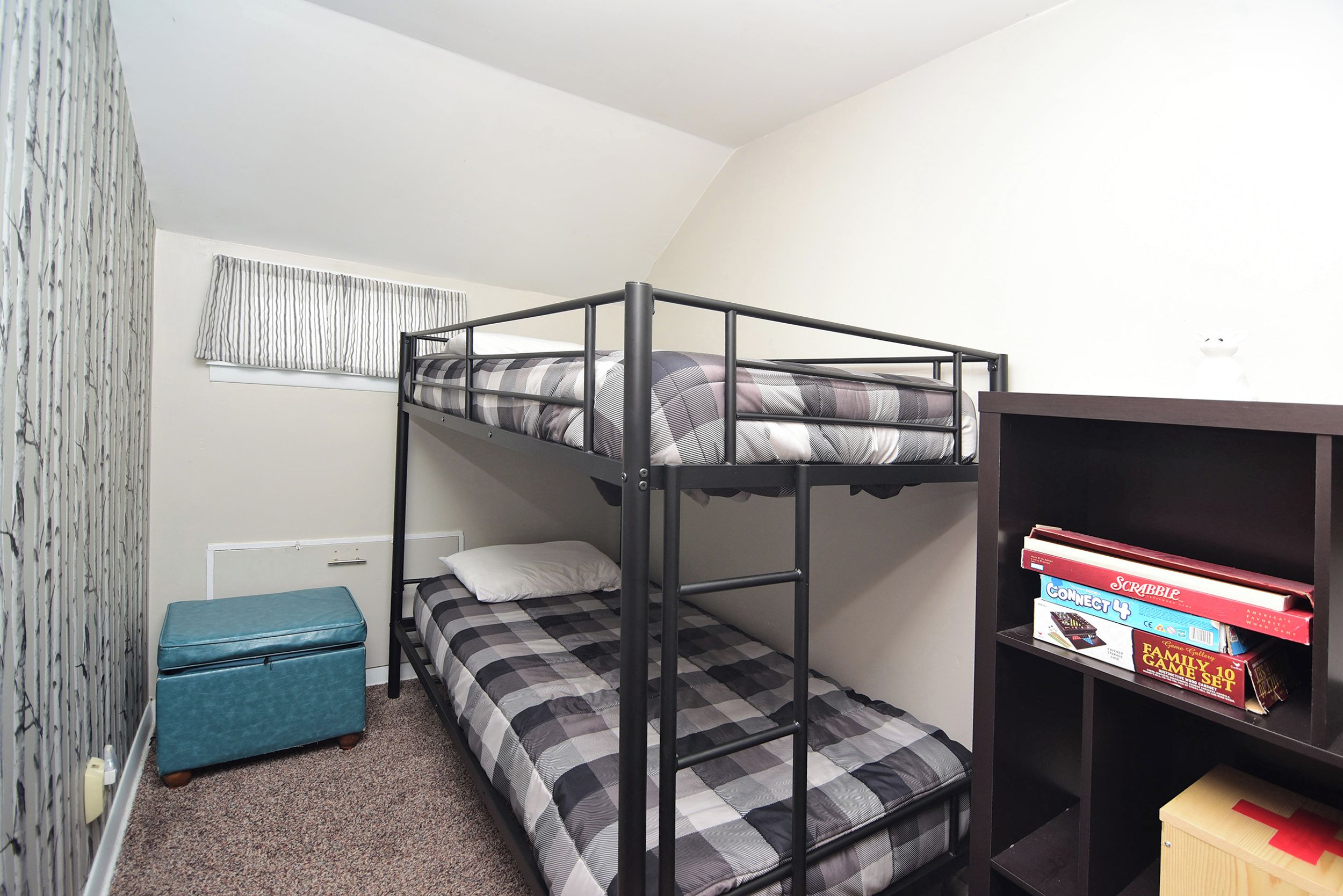 A bunk bed with a checkered bedspread, a small blue chest of drawers, and a bookshelf with board games.