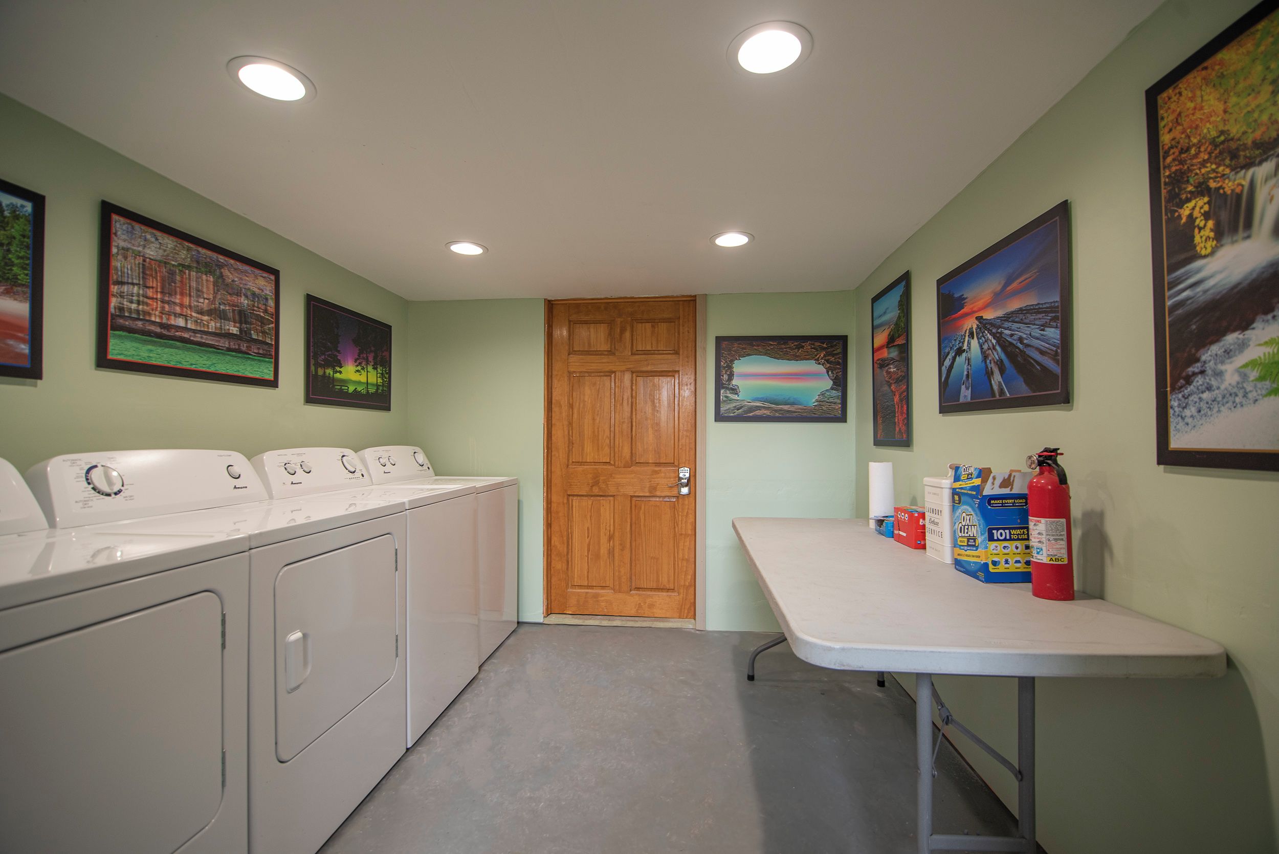 A laundry room with a wooden door, a table with cleaning supplies, and framed pictures on the walls.