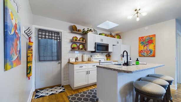 Une cuisine moderne avec des meubles blancs, un four à micro-ondes et un grand îlot central doté de tabourets.
